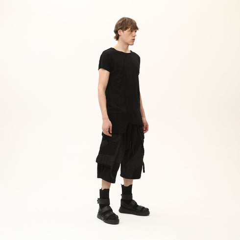Full styling view of men’s black asymmetric raw seam T-shirt for festival and streetwear outfits.