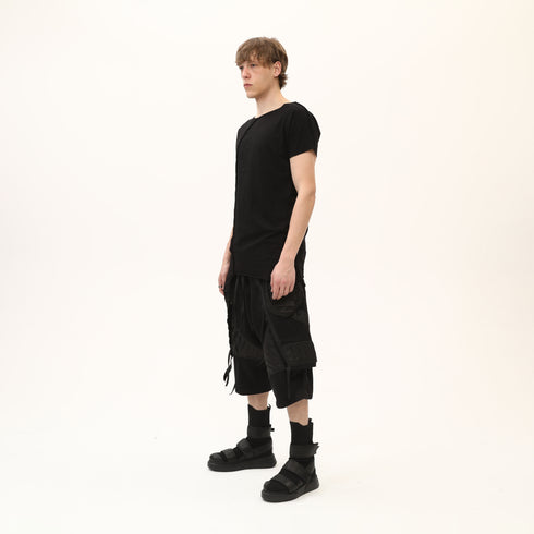 Side view of men’s black asymmetric raw seam T-shirt styled with black statement shorts.