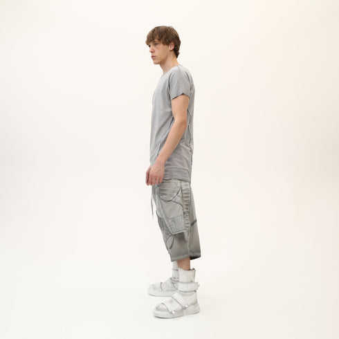 Side view of men’s grey asymmetric raw seam T-shirt styled with grey statement shorts.