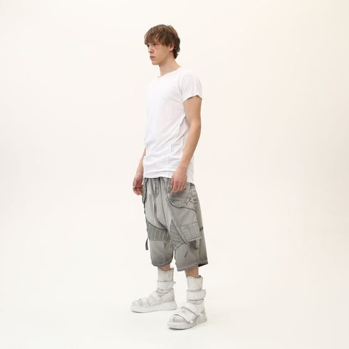 Side view of men’s white asymmetric raw seam T-shirt styled with grey statement shorts.