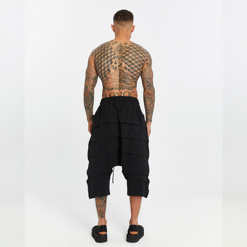 Back view of men’s black paneled drop-crotch capri pants with cropped length and bold streetwear silhouette.