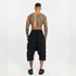 Back view of men’s black paneled drop-crotch capri pants with cropped length and bold streetwear silhouette.