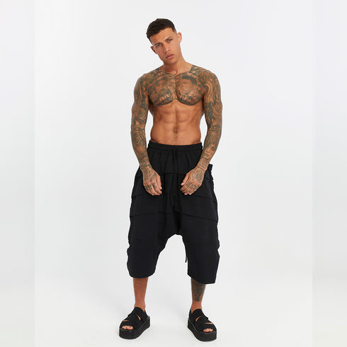 Full look of men’s black drop-crotch capri pants with front and back paneled detailing and bold festival-ready attitude.
