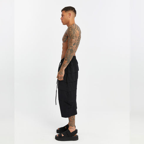 Side view of men’s black capri pants with front and back paneled construction, drop-crotch fit and side pocket detail.