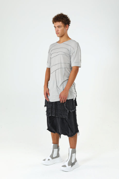 Three-quarter view of men’s grey raw seam T-shirt styled with drop-crotch capri pants for a bold streetwear look.