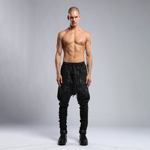 Front view of men’s black piped raw stitch shalwar pants with drop-crotch silhouette and elastic waistband.