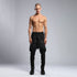 Front view of men’s black piped raw stitch shalwar pants with drop-crotch silhouette and elastic waistband.