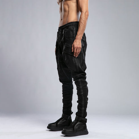 Side view of men’s black drop-crotch shalwar pants with avant-garde streetwear fit and slim lower-leg shape.